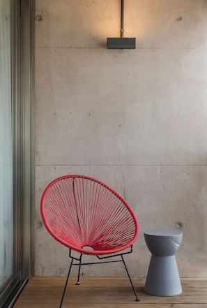 Una silla roja y un tablero gris frente a una pared de hormigón con suelo de madera.