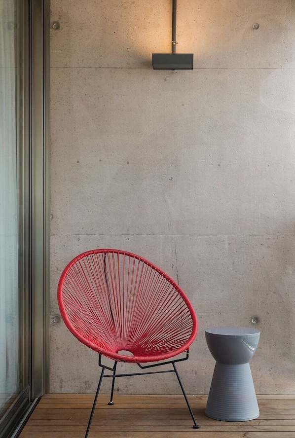 A red chair and a grey table against a concrete wall with a wooden floor.