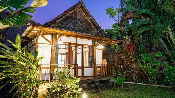 Una casa de madera tradicional con techo de paja, rodeada de exuberante vegetación tropical.