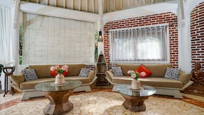 Un salón amplio con dos sofás, una mesa de centro de cristal y una pared de ladrillo.