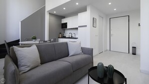 Een moderne woonkamer met een grijze bank, een klein zwart tafeltje met twee decoratieve vazen, en een trap naar een keuken.