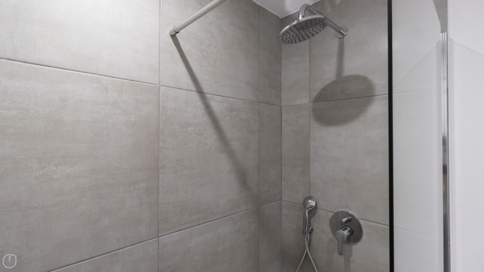 A modern shower with a handheld showerhead and a wall-mounted rain showerhead.