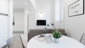 Een moderne woonkamer met een bank, een bijzettafeltje met tijdschriften, een televisie en een bord met de tekst 'PRADA MARFA'.