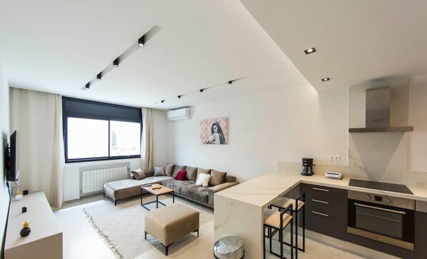 Un appartement moderne comprenant un espace de vie, une kitchenette et une grande fenĂŞtre.