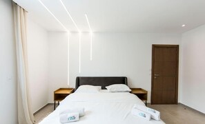 Une chambre d’hôtel avec un lit, une table de chevet en bois, une porte en bois et un rideau blanc.