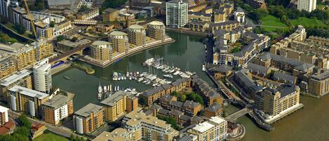 An aerial view of a riverside urban area with multiple buildings, including a prominent hotel with a waterfront terrace.