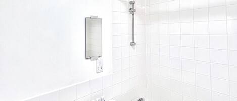 A bathroom with white tiles, a bathtub, a sink, a mirror, and a showerhead.