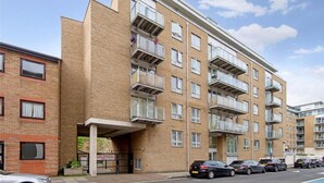 A multi-story residential building with balconies, a gated entrance, and parked cars. - Lovely 1-bed Apartment in London by the Harbour (London)