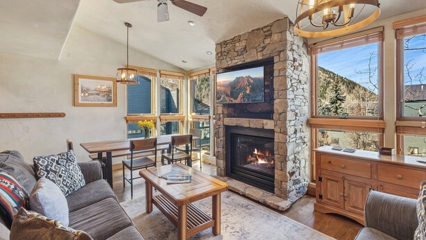 A cozy living room with a stone fireplace, a ceiling fan, and a dining area with natural light.
