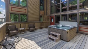 Une terrasse en bois avec un jacuzzi, des fauteuils en osier et une table.