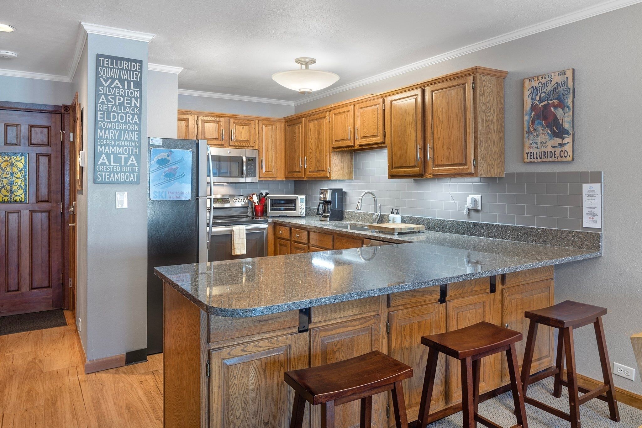 A kitchen with wooden cabinets, a granite countertop, a refrigerator, a microwave, and a coffee maker.