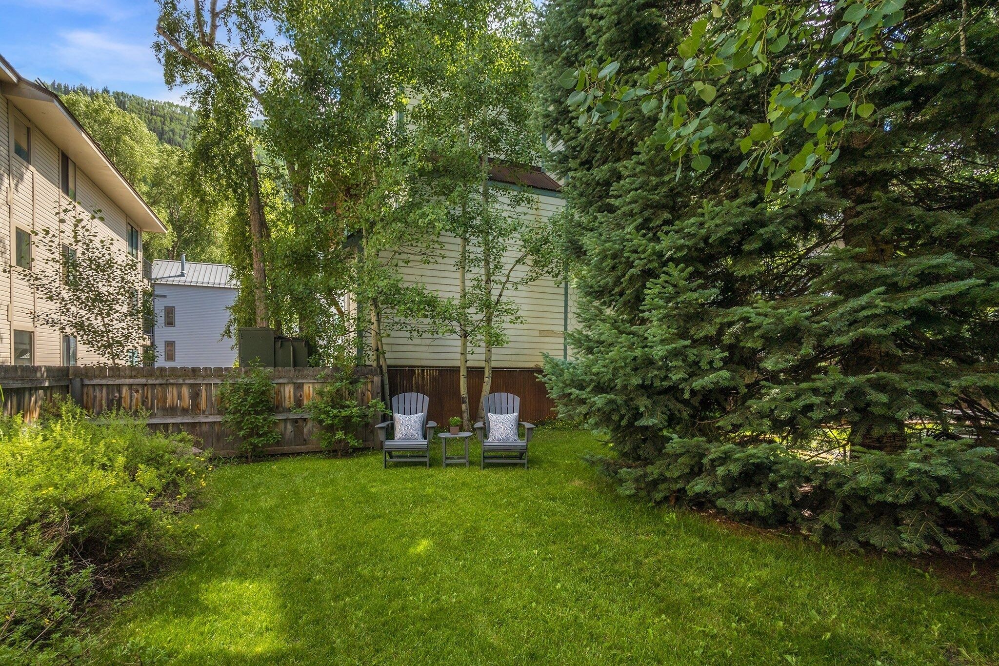 A backyard with two Adirondack chairs, a wooden fence, and a house with a sloped roof.