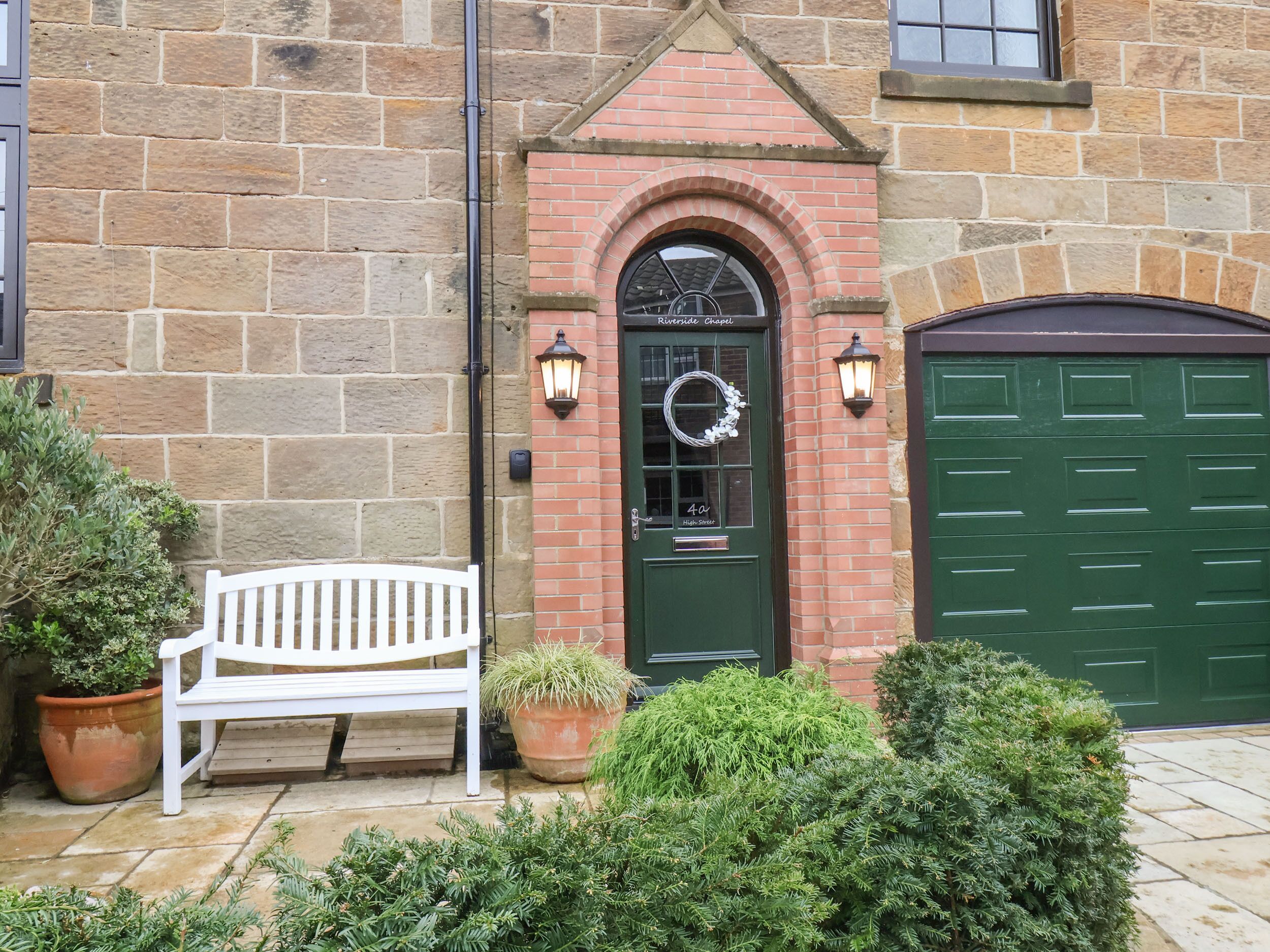 A stone building with a green door, a white bench, and potted plants.