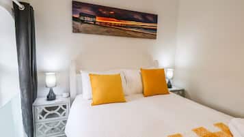 A hotel room with a large bed, two bedside lamps, a nightstand, a painting of a sunset, and a curtain.
