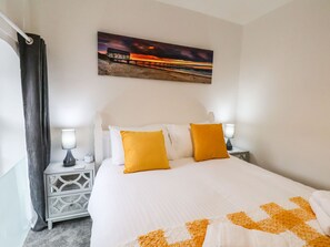 A hotel room with a large bed, two bedside lamps, a nightstand, a painting of a sunset, and a curtain. - Riverside Chapel (Middlesbrough)