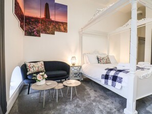 A bedroom with a four-poster bed, a dark sofa, two round tables, and a nightstand with a lamp. - Riverside Chapel (Middlesbrough)