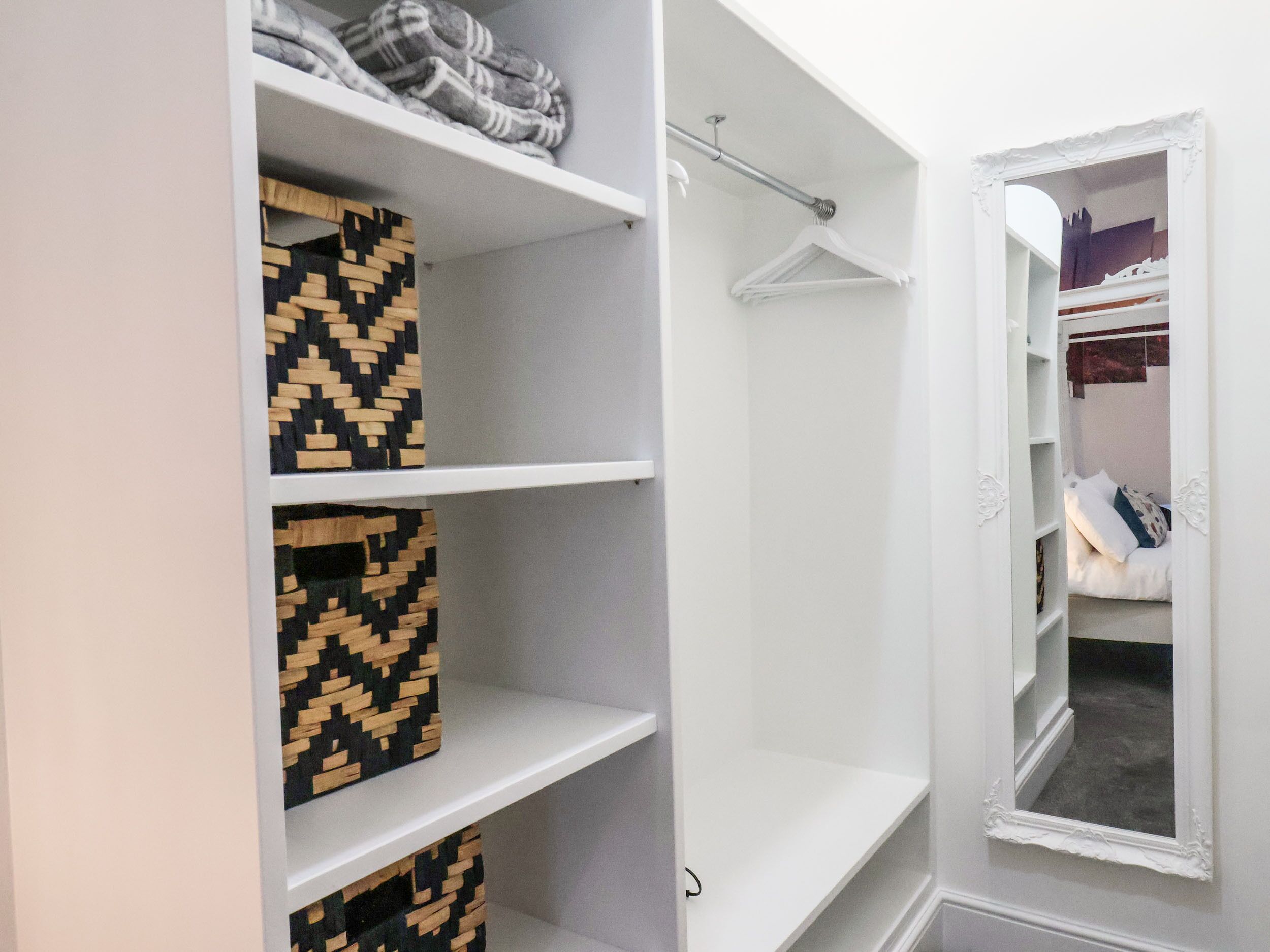A walk-in closet with open shelves, a hanging rod, and a mirror.