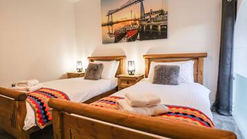 A hotel room with two wooden beds, each with a headboard, white linens, and a colorful blanket. There is a painting of a bridge on the wall above the beds.