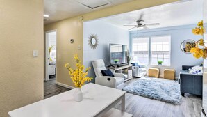 A modern living room with a white sofa, a grey armchair, a TV, and a ceiling fan. - Galveston Retreat w/ Backyard & Patio! (Galveston)