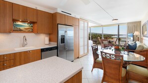 Une cuisine moderne avec des meubles en bois, un réfrigérateur en acier inoxydable et un coin repas doté de meubles en osier.