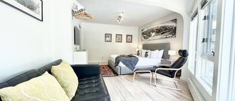 A modern bedroom with a bed, a black leather sofa, a chair, and a large window.