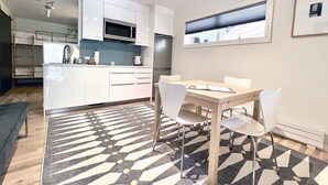 A modern kitchen with white cabinets, a microwave, and a refrigerator. There is a dining area with a table and chairs, and a patterned rug on the floor. - Chic, Modern Walk Anywhere @ Viking Lodge 206 1 Bedroom Condo by RedAwning (Telluride)