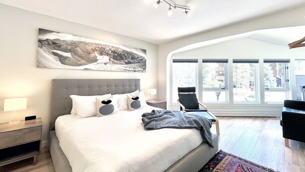 A modern bedroom with a large bed, a headboard, a nightstand, a desk, and a large window with a view. - Chic, Modern Walk Anywhere @ Viking Lodge 206 1 Bedroom Condo by RedAwning (Telluride)