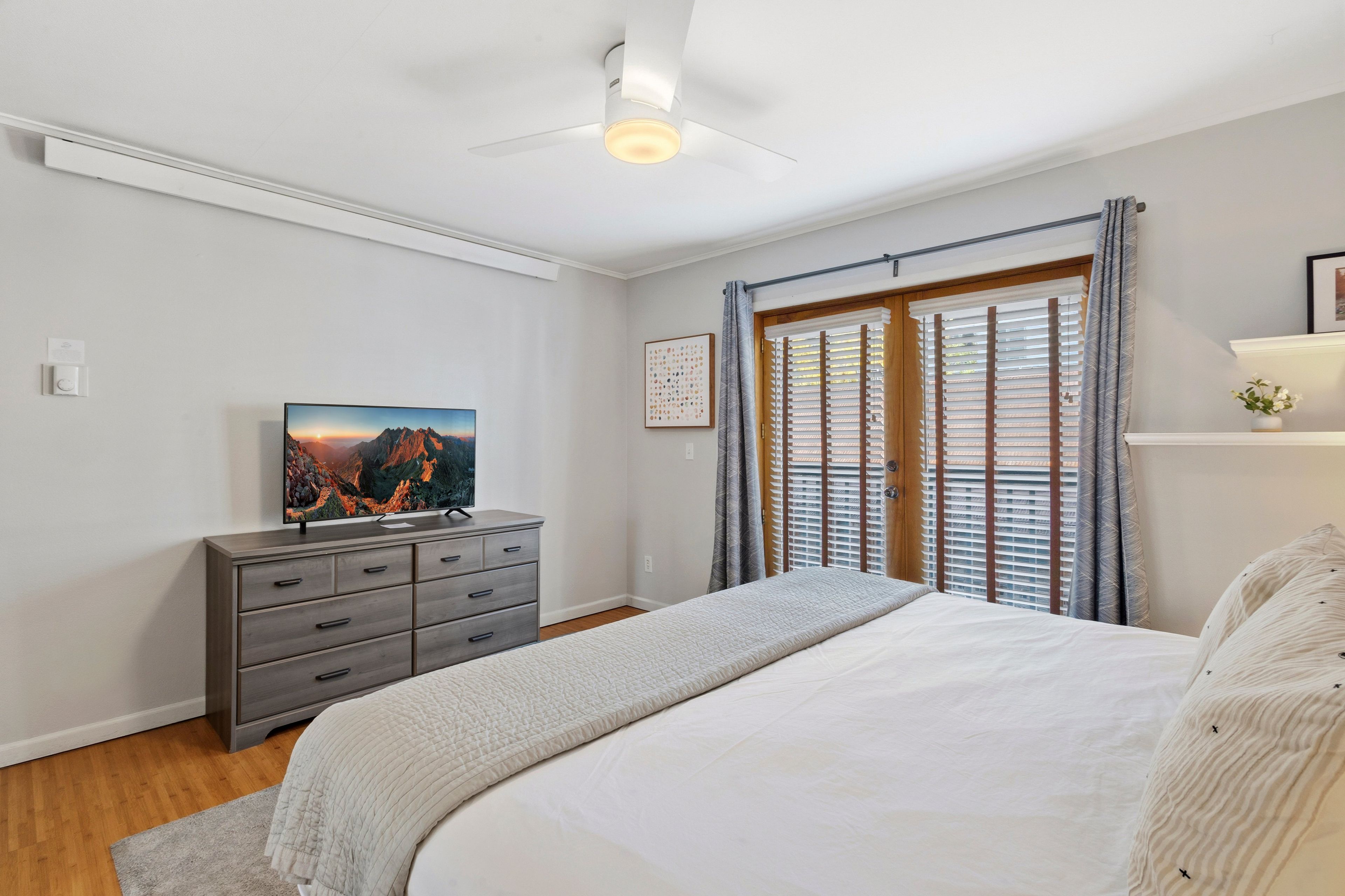 A bedroom with a bed, a dresser, a painting, a ceiling fan, and a window with blinds.
