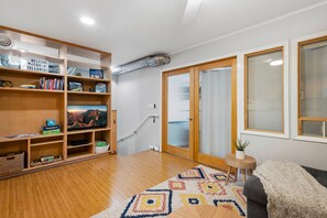 A modern living room with a wooden floor, a large bookshelf, a flat-screen TV, a patterned rug, and a sliding glass door leading to a balcony.