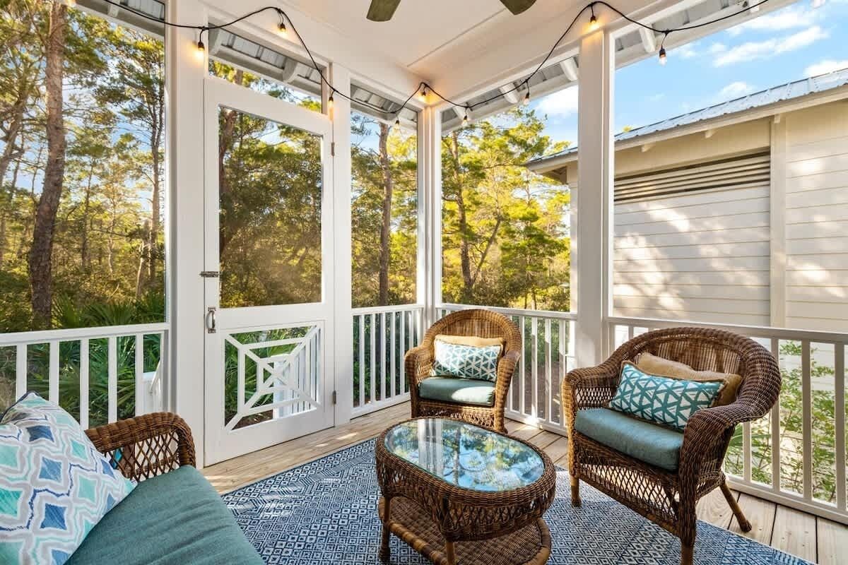 A covered porch with wicker furniture, a glass table, and string lights.