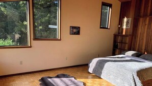 A bedroom with a large window, a bed with a gray blanket, and a wooden floor. - *Ten Trees* Cabin, Secluded, Near Redwood Parks (Myers Flat)