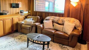 A cozy cabin interior with a wooden interior, a leather sofa, a small round table, and a TV mounted on the wall. - *Ten Trees* Cabin, Secluded, Near Redwood Parks (Myers Flat)