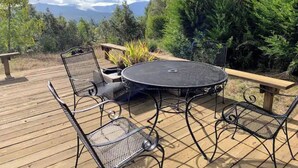 A deck with a round table and metal chairs, surrounded by greenery and a mountain view. - *Ten Trees* Cabin, Secluded, Near Redwood Parks (Myers Flat)