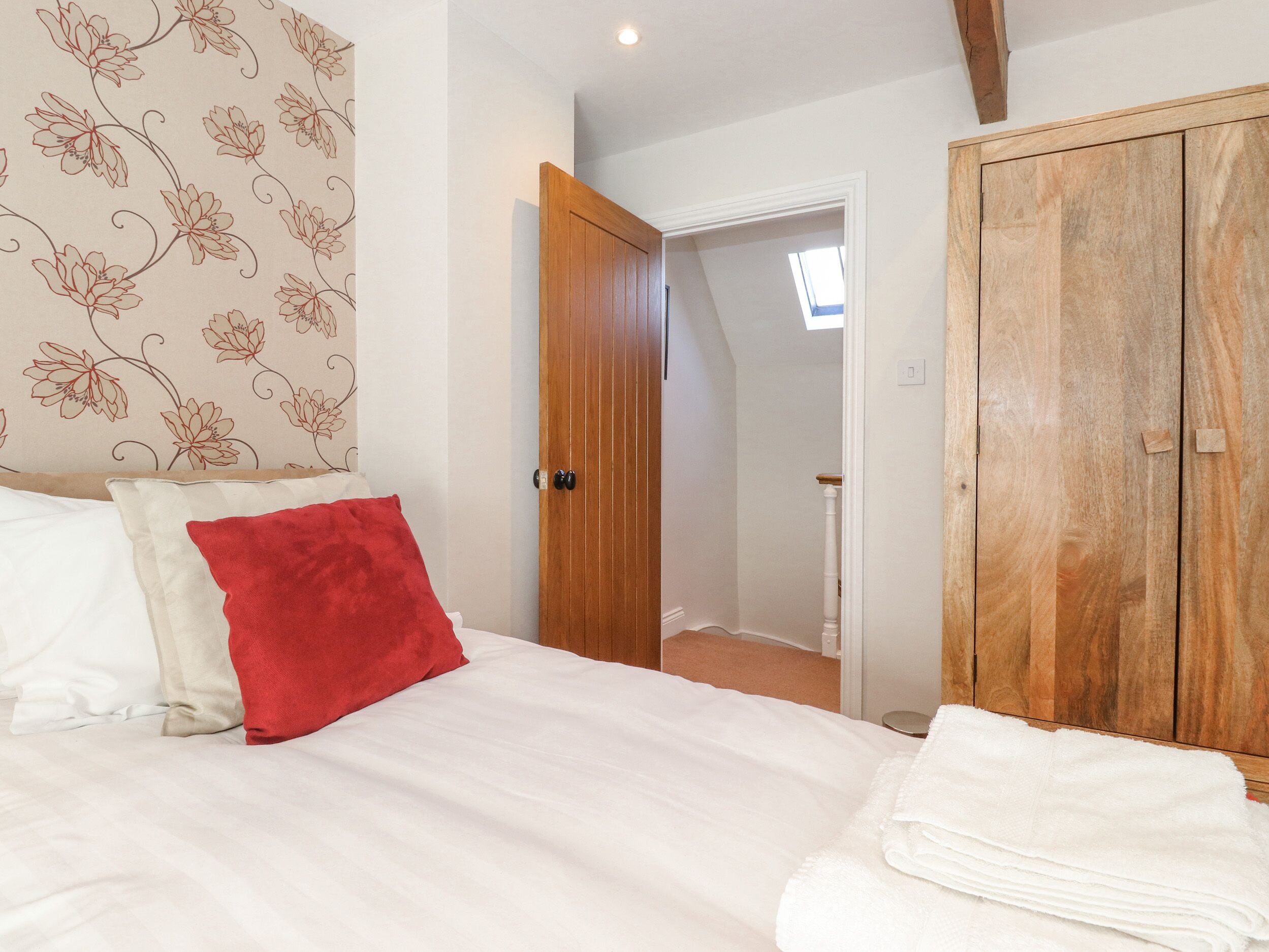 A bedroom with a bed, a red pillow, a white pillow, a wooden wardrobe, and a door leading to another room.