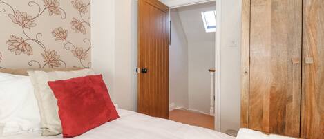 A bedroom with a bed, a red pillow, a white pillow, a wooden wardrobe, and a door leading to another room.