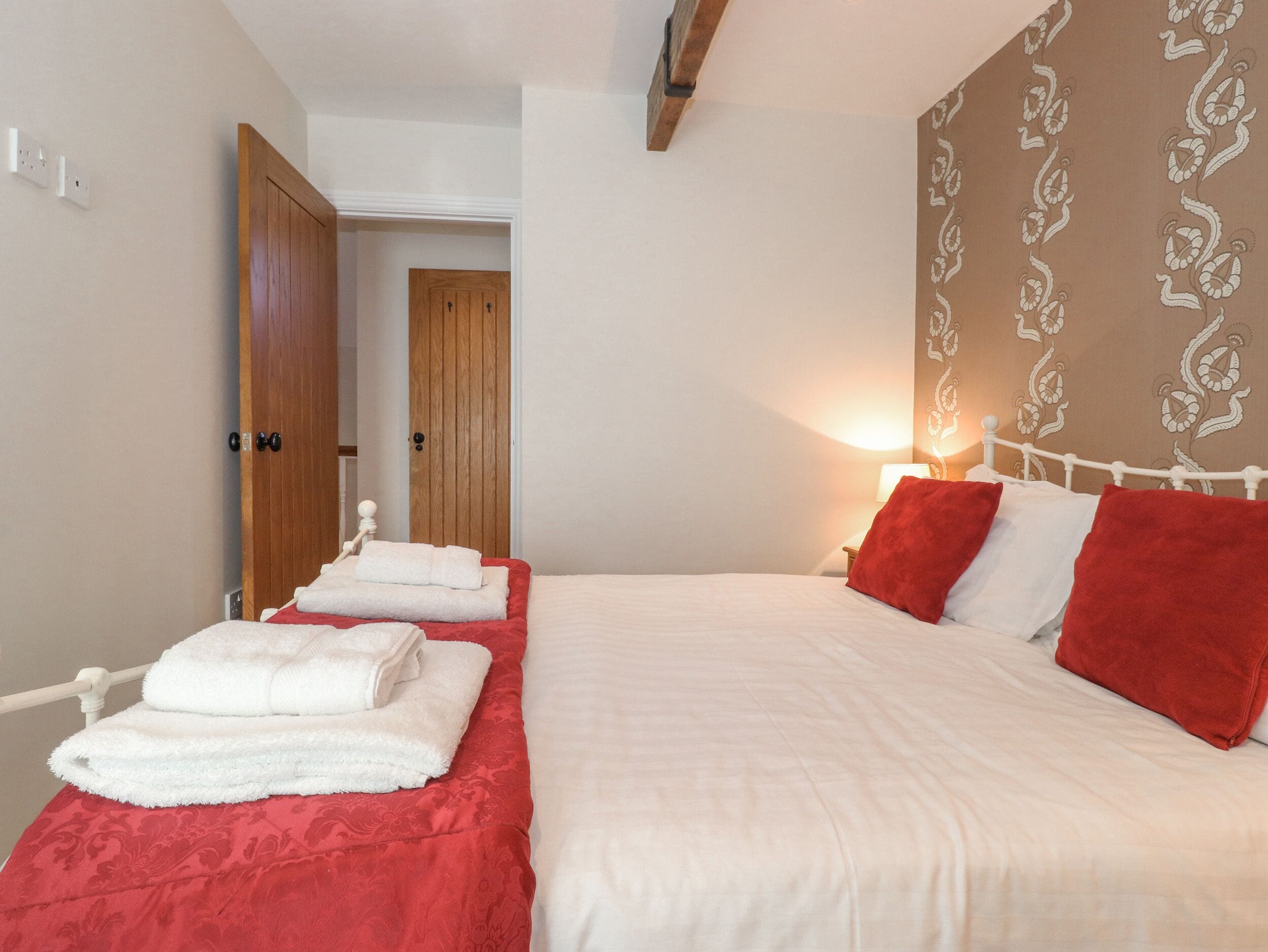 A hotel room with two beds, each with red and white bedding, and a wooden wardrobe.