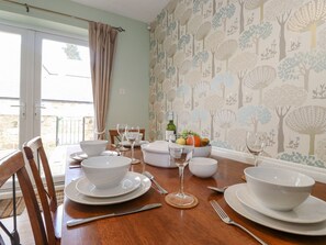 A dining table set with white dishes, glasses, and cutlery, with a fruit bowl and a bottle on the table. - Willow Cottage (Alnwick)