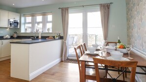 A modern kitchen with a central island, dining table with chairs, and a balcony with curtains. - Willow Cottage (Alnwick)