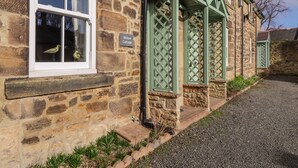 A stone cottage with a 'Willow Cottage' sign, a window with a bird decoration, and a gravel path. - Willow Cottage (Alnwick)