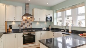 A kitchen with white cabinets, a black countertop, a stainless steel range hood, a built-in oven, and a window with a view of the outside. - Willow Cottage (Alnwick)
