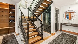 A modern staircase with wooden steps and glass railings, leading to a room with a large mirror and a wooden console. - Luxury Townhome On Depot. 3 Mins Walk To Main St/gondola. Heated Garage, Private Roof Top Hot Tub. 4 Bedroom Townhouse by RedAwning (Telluride)