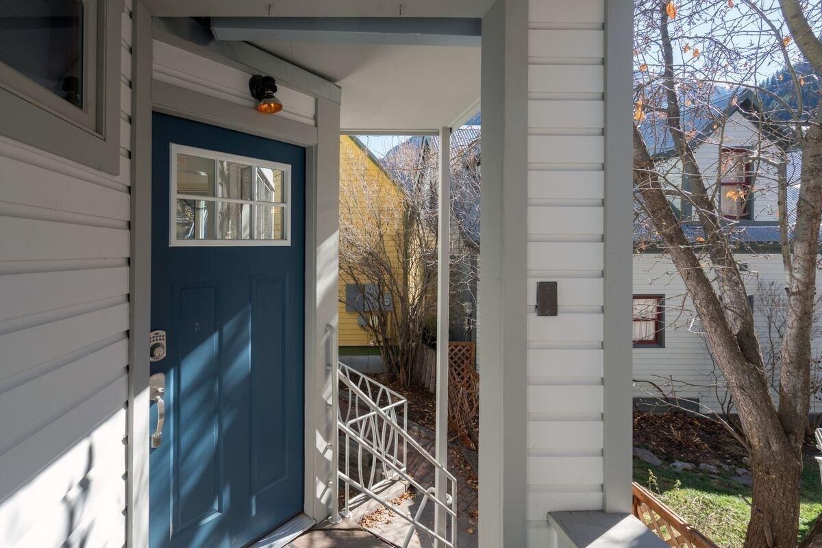 A blue door with a window, a white railing, and a view of a yard with trees and a building in the background.