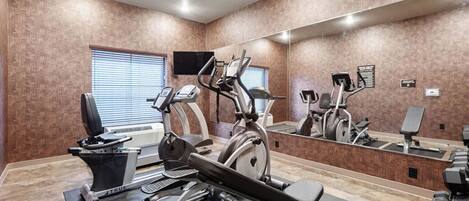 Un gimnasio con máquinas de cardio, pesas libres y un espejo grande.