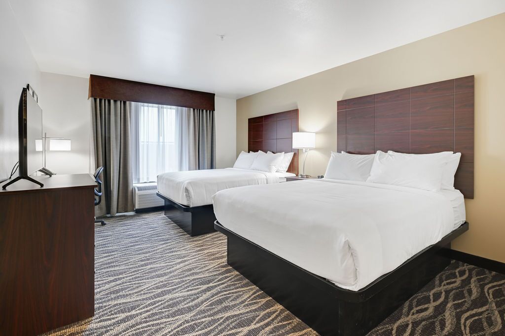 A hotel room with two beds, a desk, a mirror, and a window with curtains.