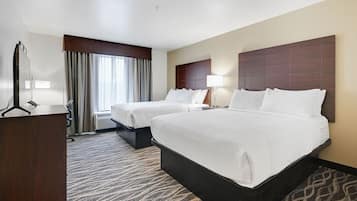 A hotel room with two beds, a desk, a mirror, and a window with curtains.