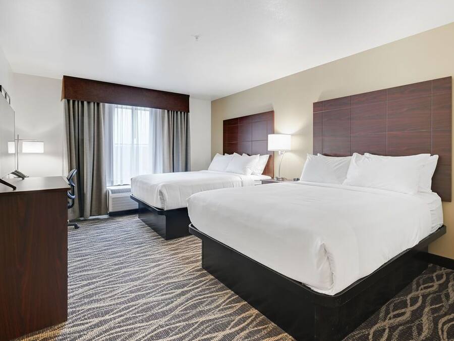 A hotel room with two beds, a desk, a mirror, and a window with curtains.