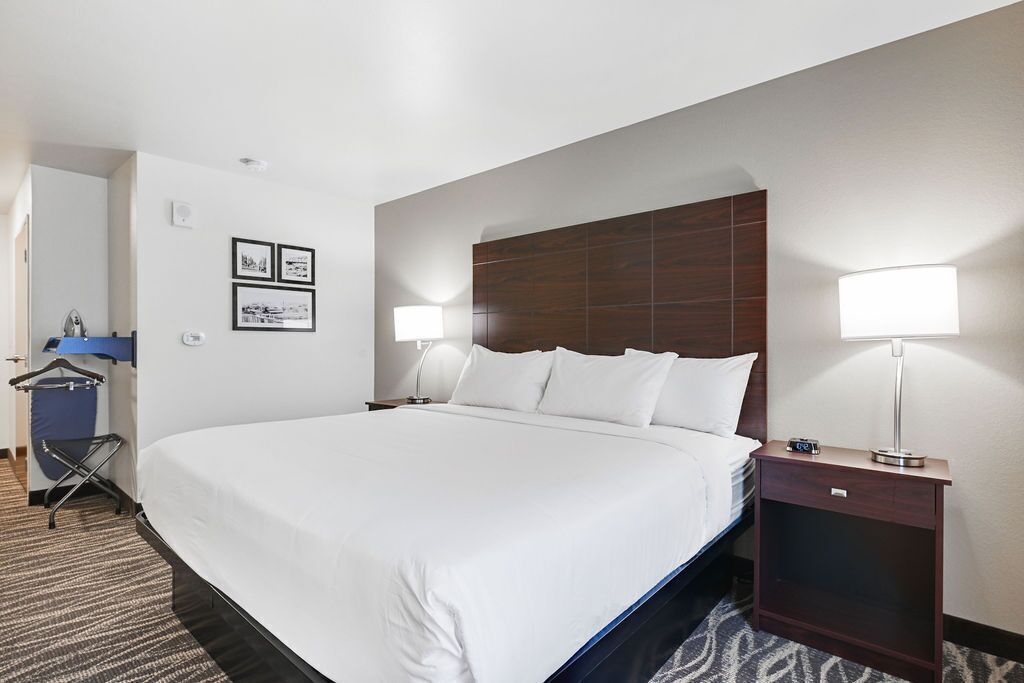 Ein Hotelzimmer mit einem großen Bett, zwei Nachttischlampen, einem Holz-Kopfteil, einem kleinen Nachttisch und einem an der Wand hängenden Bilderrahmen.