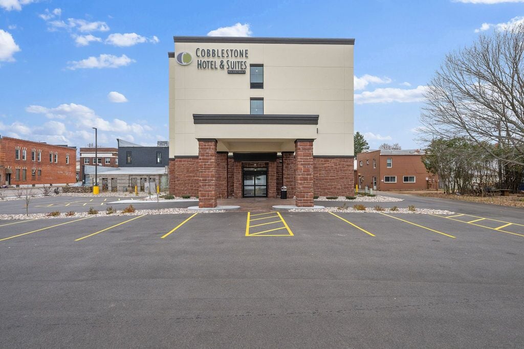 A Cobblestone Hotel & Suites with a modern design, featuring a brick facade and a parking lot with marked spaces.