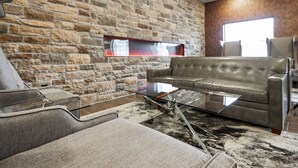A modern living room with a stone wall, a leather sofa, a glass coffee table, and a large window. - Cobblestone Hotel & Suites - Central Wisconsin Airport (Mosinee)