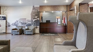 A hotel reception area with a modern design, including a reception desk, seating area, and a cityscape mural on the wall. - Cobblestone Hotel & Suites - Central Wisconsin Airport (Mosinee)
